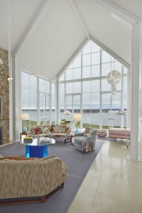 The living room addition in this Shelter Island residence was designed with a high peaked roof and walls of windows positioned to take full advantage of bay views. The home features two Edward Wormley corner sofas for Dunbar, of similar shape but slightly different proportions. Swivel chairs, also by Wormley, are covered in light-blue velvet and are arranged around a coffee table in the shape of an eye designed by Nicola L. (Credit: Courtesy of The Monacelli Press / Anastassios Mentis)