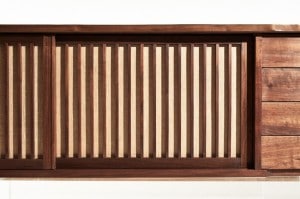 The backing behind the grills of the sliding walnut doors on the console's right side is made from woven pandanus cloth, which is sourced from the tropical pandan tree, also known as a screw pine or screw palm.